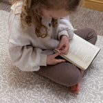 Toddler sits on The Acorn Playmat by Totter + Tumble x Morris & Co. - a luxury padded play mat featuring non-toxic foam and elegant William Morris Acorn motifs.