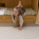 A child plays on a decorative foam play mat by Totter + Tumble in a neutral toned nursery
