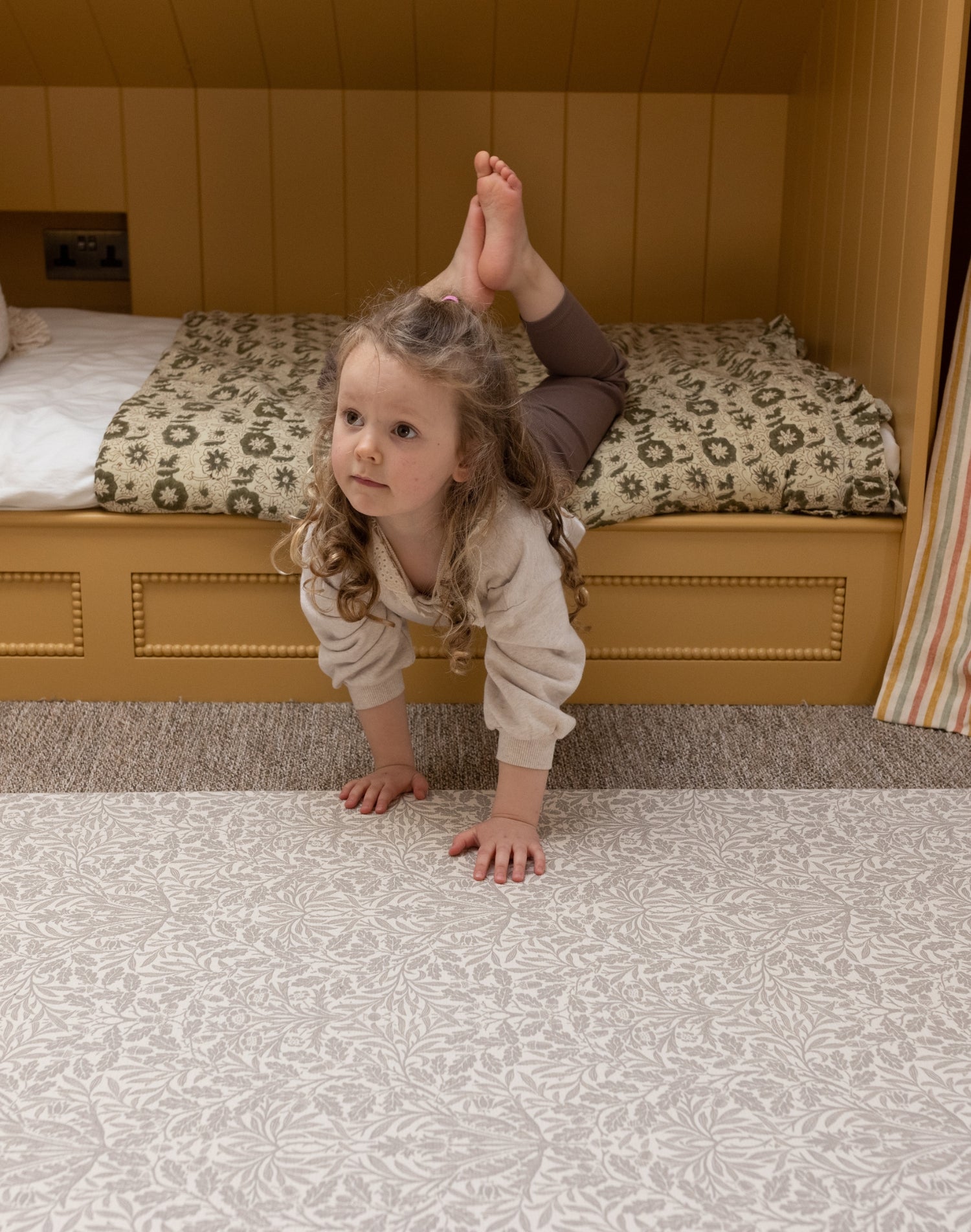 A child plays on a decorative foam play mat by Totter + Tumble in a neutral toned nursery