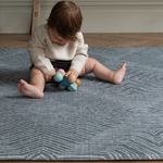 Little baby sits supported on the modern play mat by totter and tumble with a rug like design in dark charcoal made for modern homes