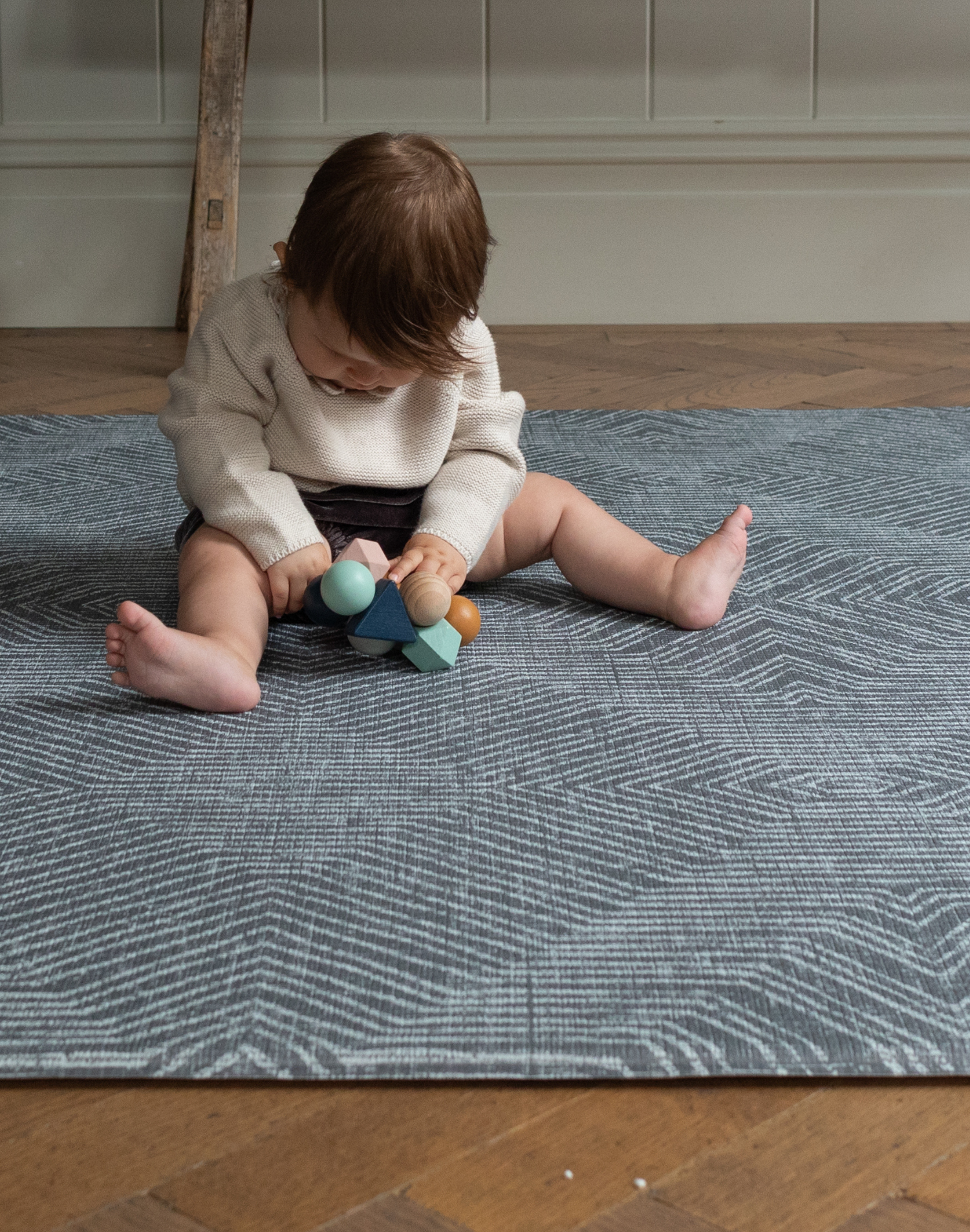 Little baby sits supported on the modern play mat by totter and tumble with a rug like design in dark charcoal made for modern homes
