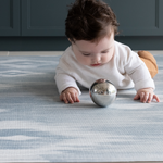 Baby playing with sensory ball on Playroom mats by Totter and Tumble in stylish designs The Atlas has a beautiful ikat design in natural tones of blue and beige