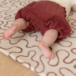 Baby on The Brecon play mat, a soft, earthy tone crawling mat with a hiking trail motif inspired by Welsh heritage.