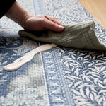 Detailed view of the durable Totter + Tumble nursery Brook play mat with nature-inspired patterns and high-end Morris & Co. craftsmanship. A hand and muslin cloth wipe up a spill on the playmat with ease.