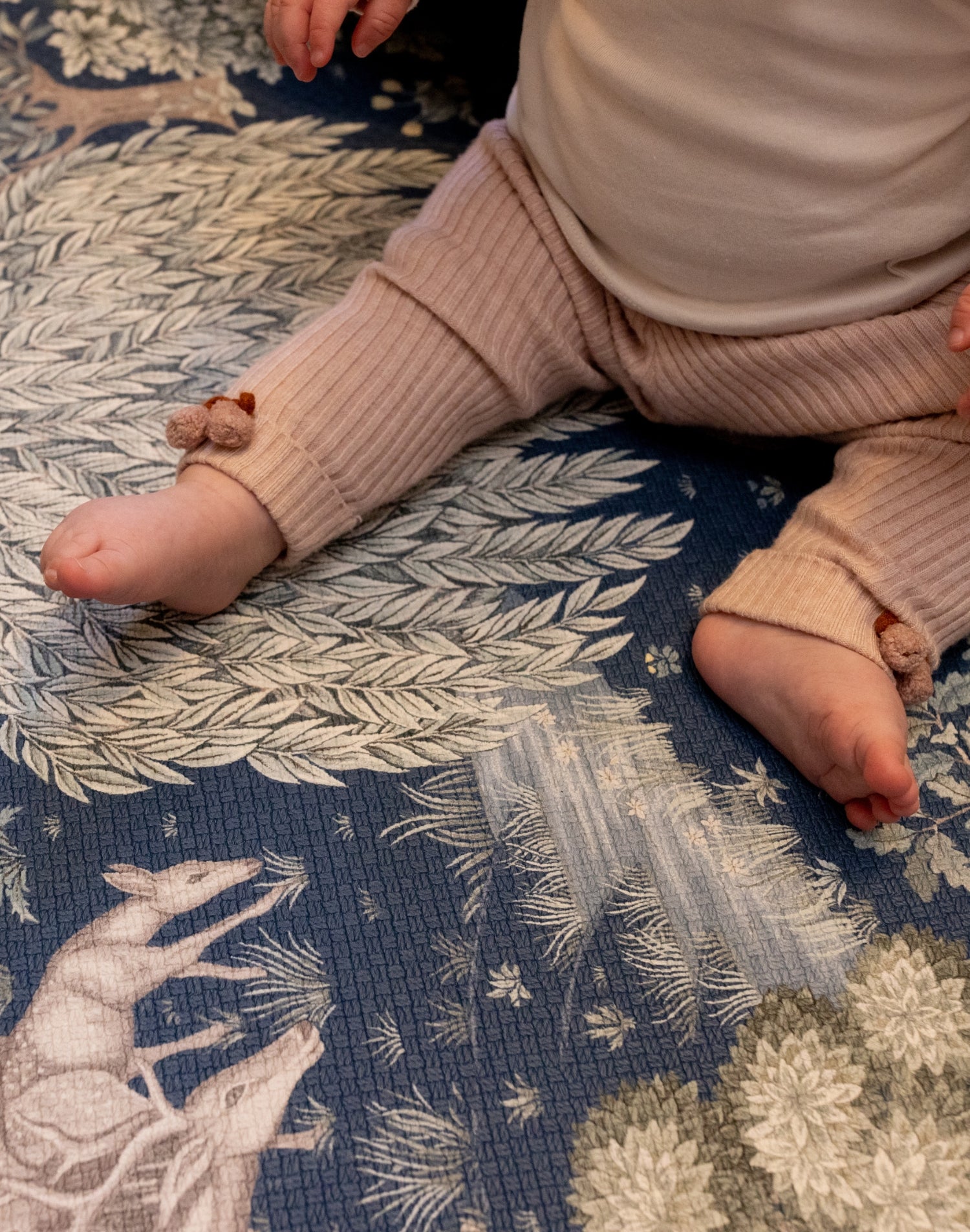 Close-up of baby’s legs during tummy time on a Totter + Tumble woodland play mat; a safe, decorative foam play mat for lovers of premium baby products.