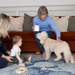 Stylish family setting with baby, mum, grandma and dog playing on a Totter + Tumble luxury playmat - a family-friendly interior essential with a two-sided luxury design.