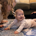 Baby smiling on a non-toxic foam play mat with classic woodland prints from the Totter + Tumble x Morris & Co. collection -safe and chic for tummy time.