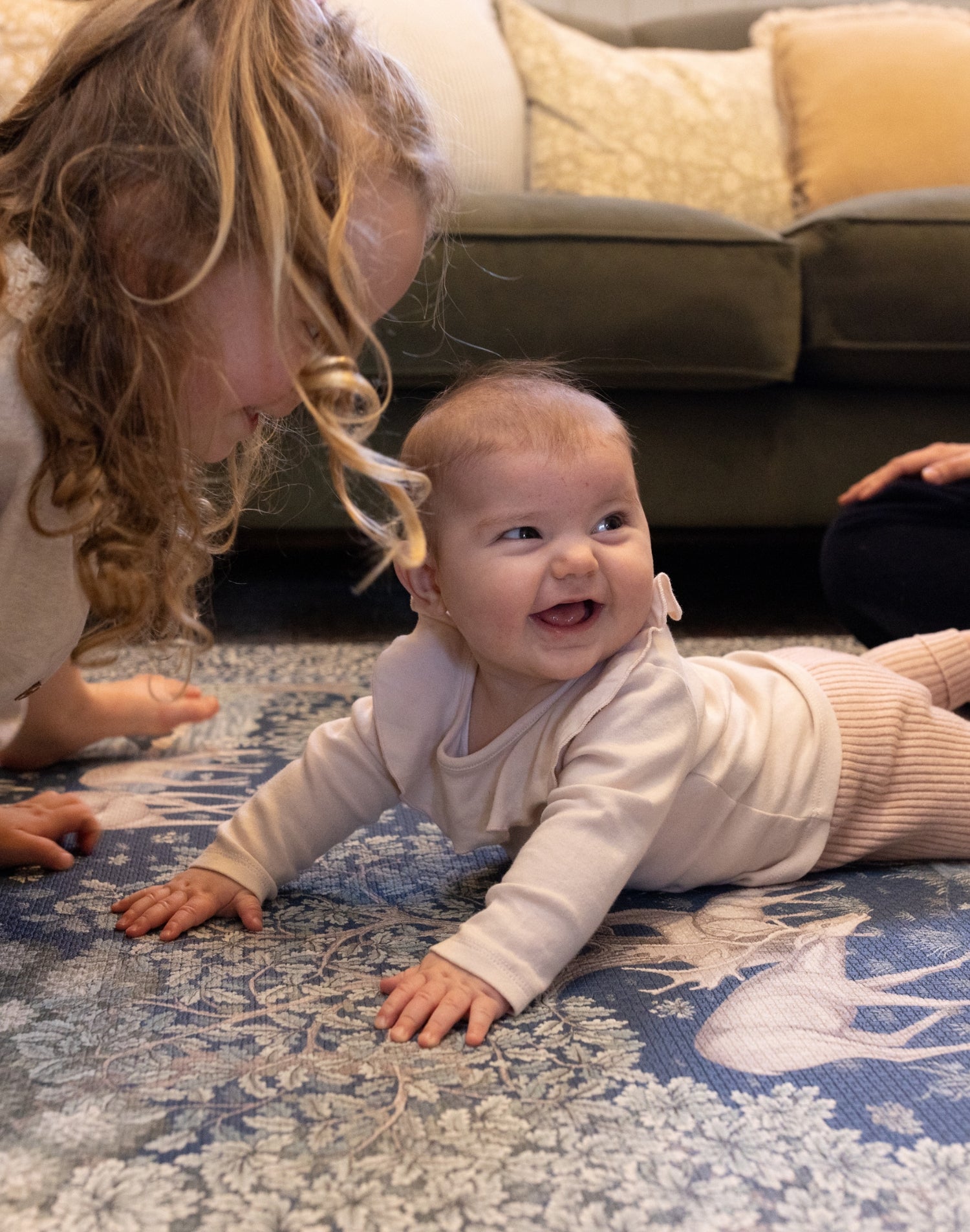 Baby smiling on a non-toxic foam play mat with classic woodland prints from the Totter + Tumble x Morris & Co. collection -safe and chic for tummy time.