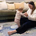 Parent supports standing baby on a luxury nursery play mat in warm woodland hues - a timeless, practical yet stylish baby product.