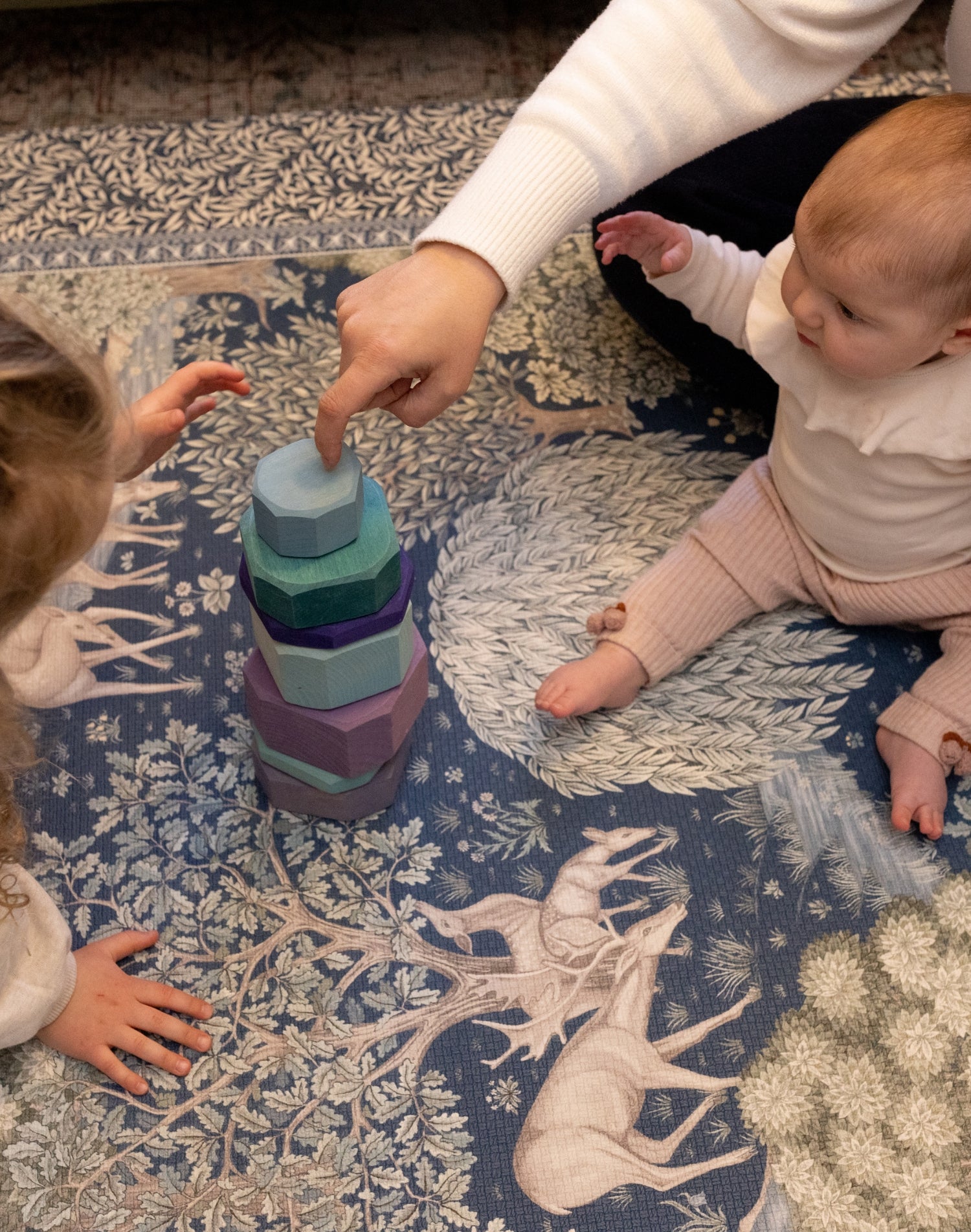 Children play with wooden stacking toys on a botanical-patterned playmat by Totter + Tumble - the perfect mix of safe play and designer nursery decor.