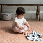 Baby reaches for sensory muslin supported on kids playmat with a warm terracotta kilim pattern