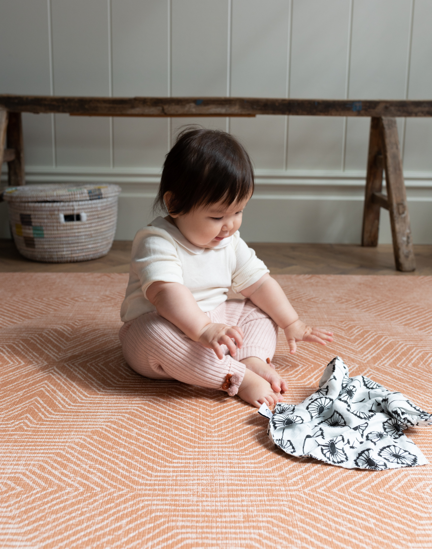 Baby reaches for sensory muslin supported on kids playmat with a warm terracotta kilim pattern
