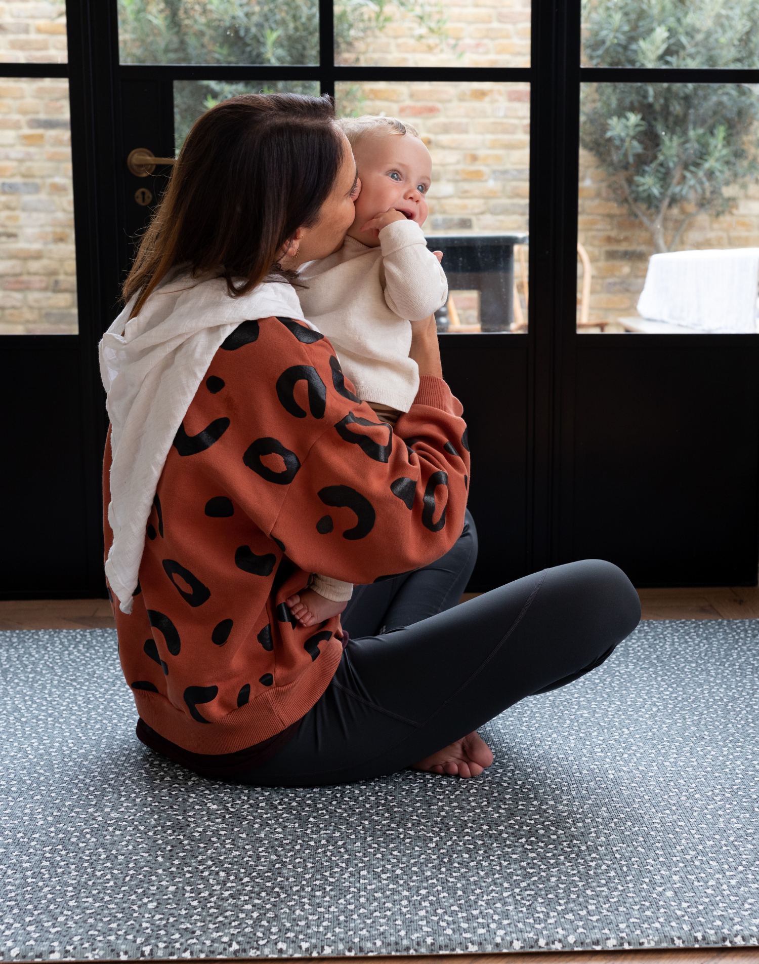 Mother holds baby sitting comfortably on the antibacterial playmat by totter and tumble