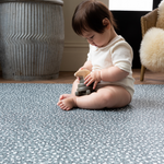 Baby girl plays with wooden toy on the green padded playmat design to protect from tumbles