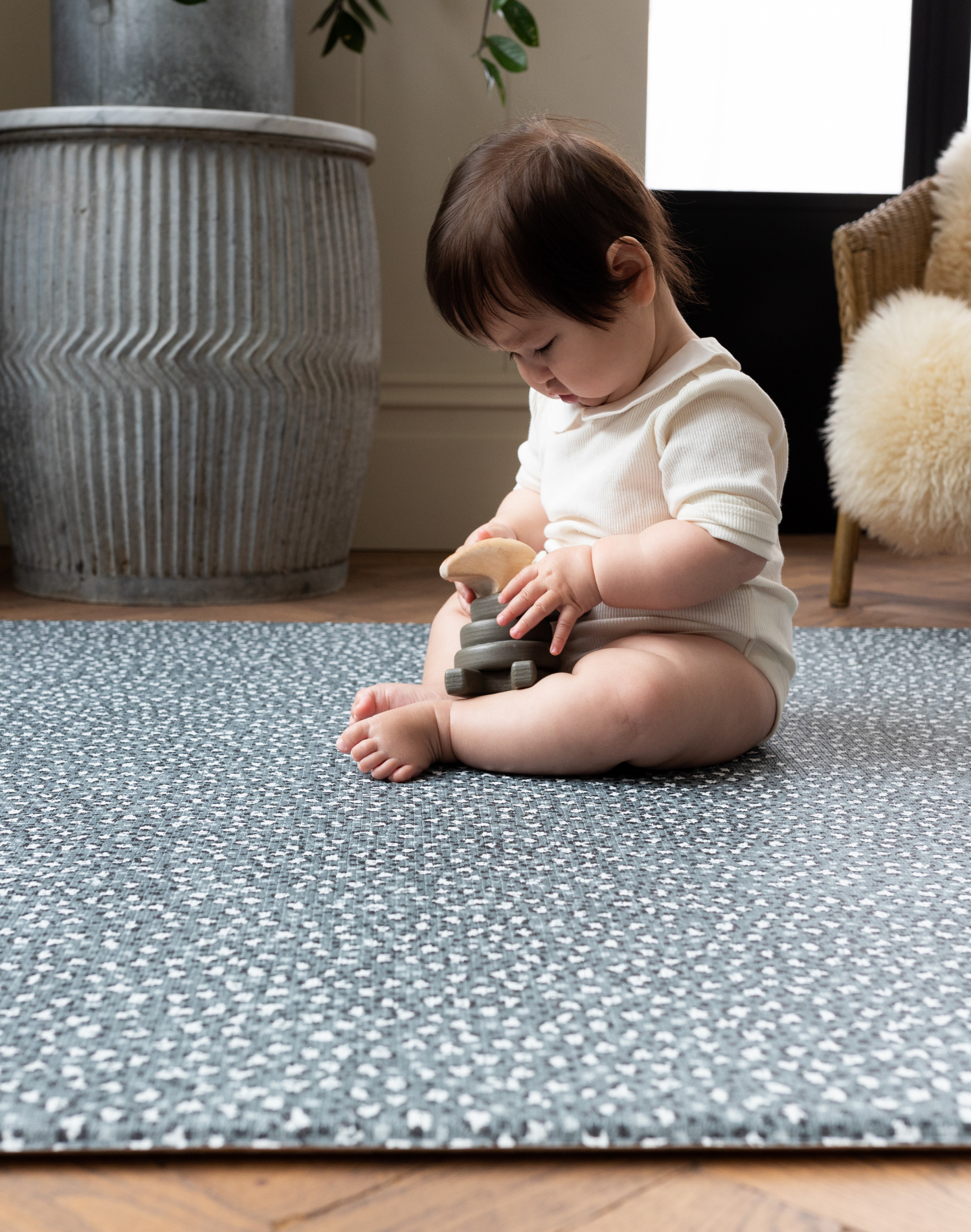 Baby girl plays with wooden toy on the green padded playmat design to protect from tumbles
