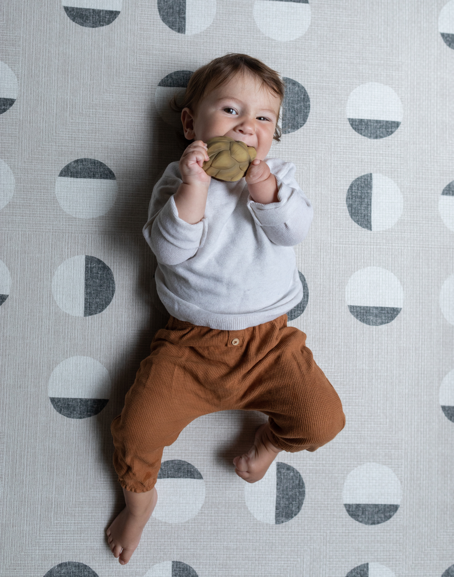 Baby chews on a teether and lays on textured baby play mat that provides support for all types of floor play