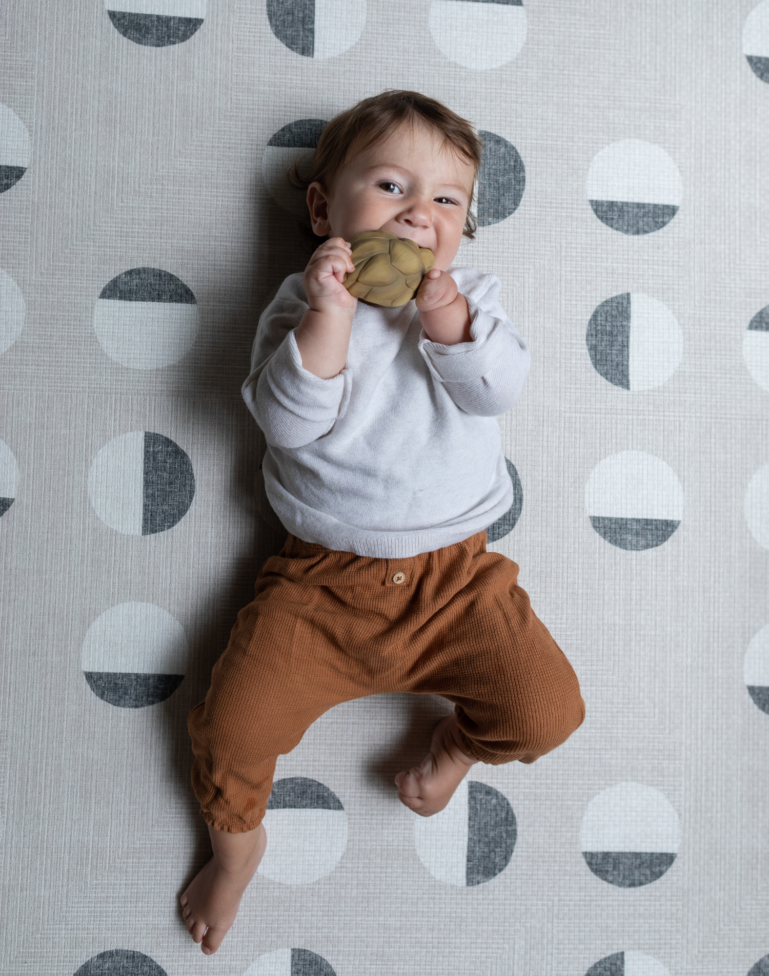 Baby chews on a teether and lays on textured baby play mat that provides support for all types of floor play