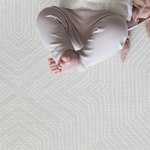 Little feet are pointing up into the air while a baby relaxes on the near neutral play mat with a subtle kilim design