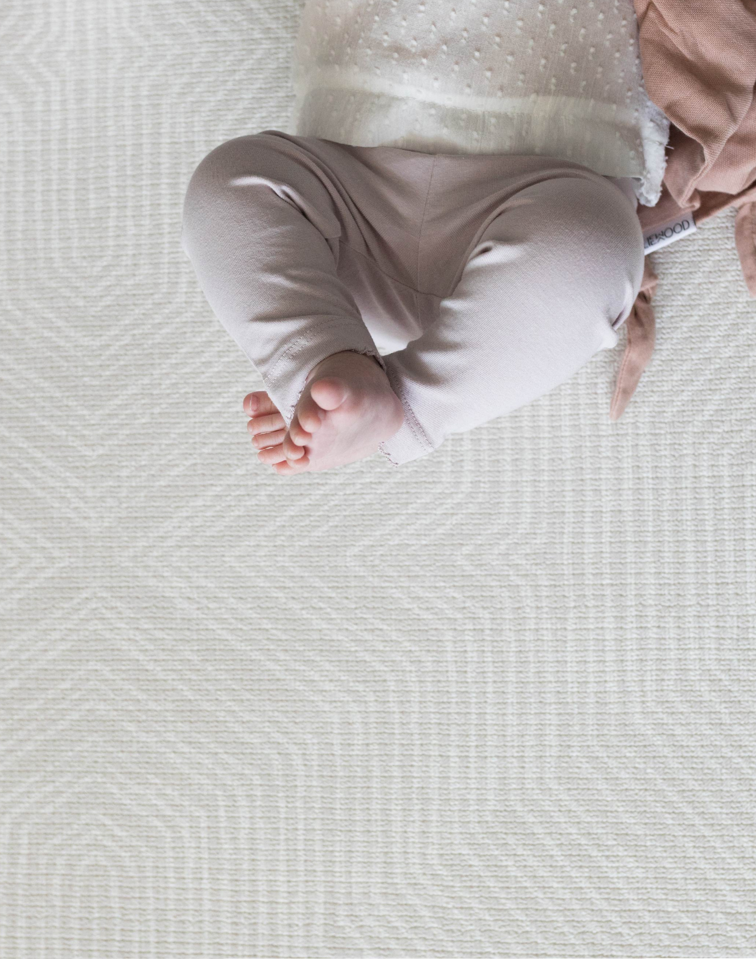 Little feet are pointing up into the air while a baby relaxes on the near neutral play mat with a subtle kilim design