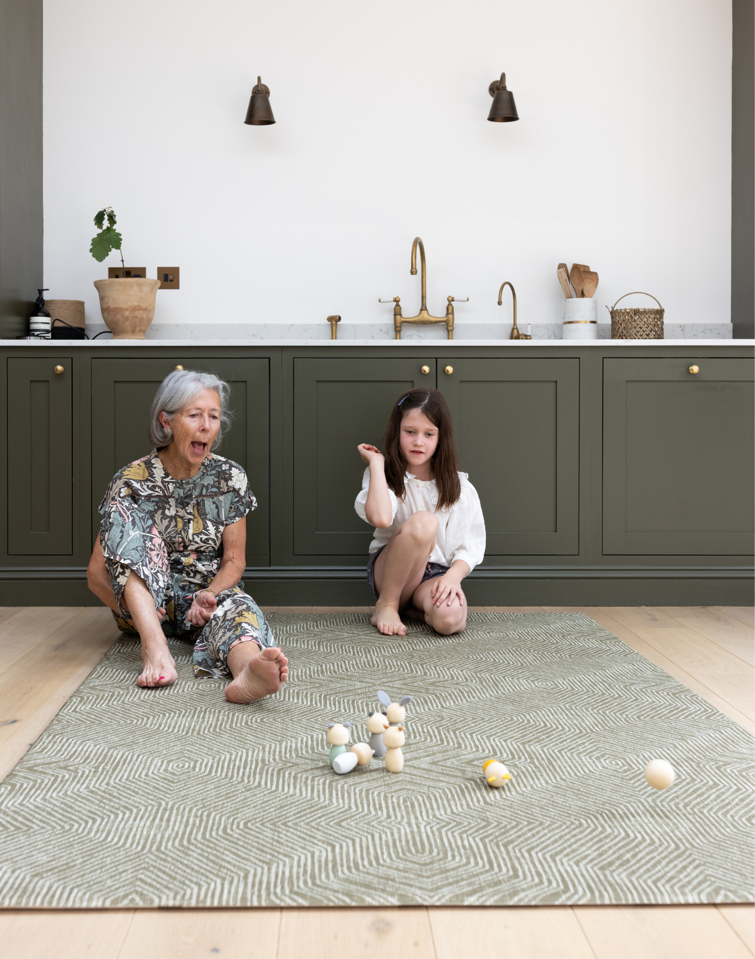 Grandmother and child sit on a large kitchen mat that has a modern kilim textile design to complement the interior