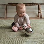 Baby engaged in shiny sensory toys sitting comfortably on green play mat with beautiful kilim textile motif