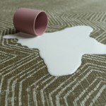 Cup of milk spills on green baby play mat with a sealed surface to make cleaning easier