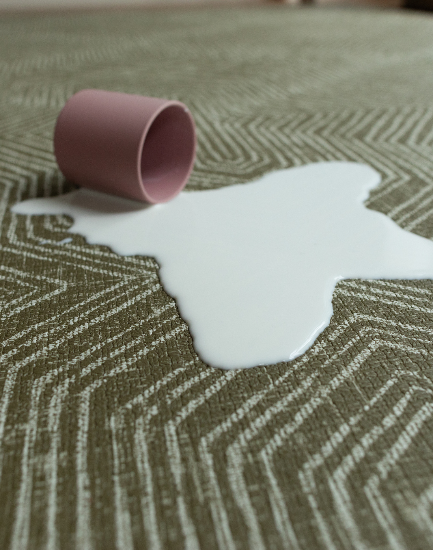 Cup of milk spills on green baby play mat with a sealed surface to make cleaning easier