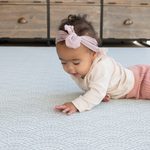 Baby lays on tummy on floor mat interested in the beautiful scalloped motif inspired by Japanese Seigaiha waves