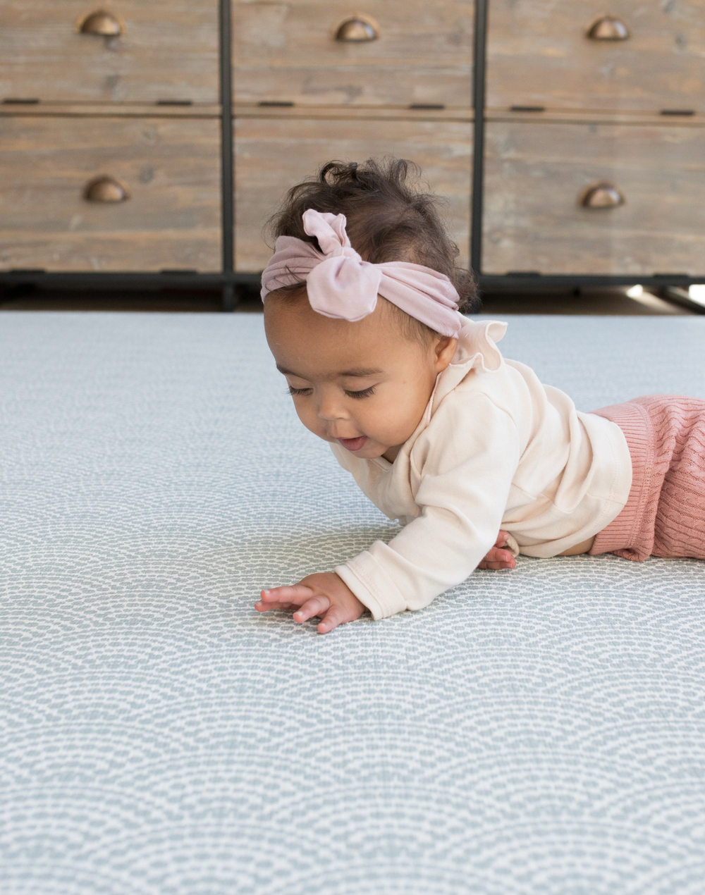 Baby lays on tummy on floor mat interested in the beautiful scalloped motif inspired by Japanese Seigaiha waves