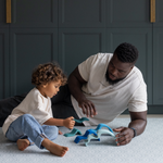 Father and son sitting comfortably on thick play mat designed with memory foam for protection on hard floors playing with wooden Grimms toys