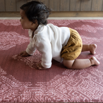 Baby crawling on deep red play mat with intricate batik inspired detailing memory foam provides support for knees and crawling babies