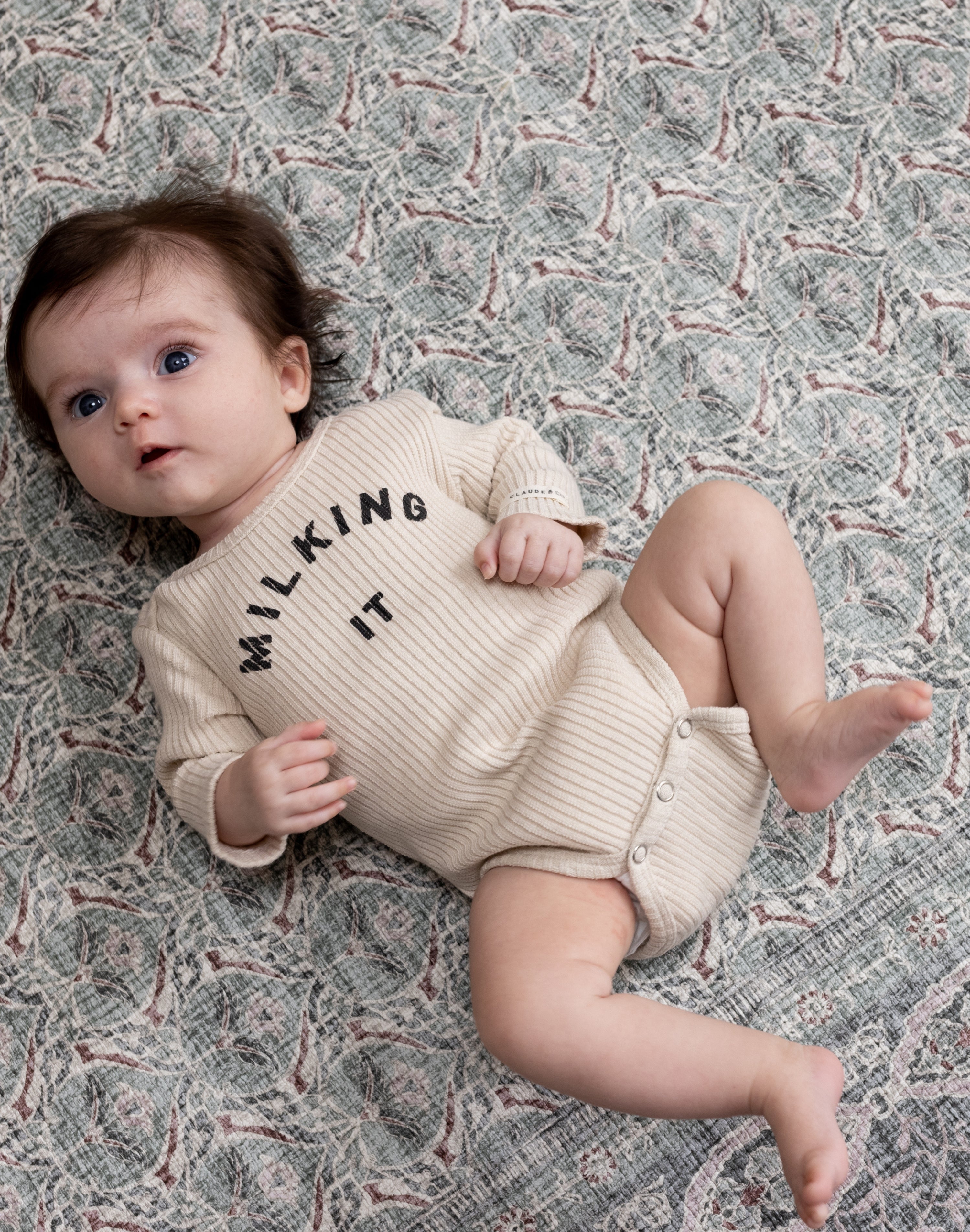 Baby lying happily on patterned green Totter + Tumble baby rug playmat
