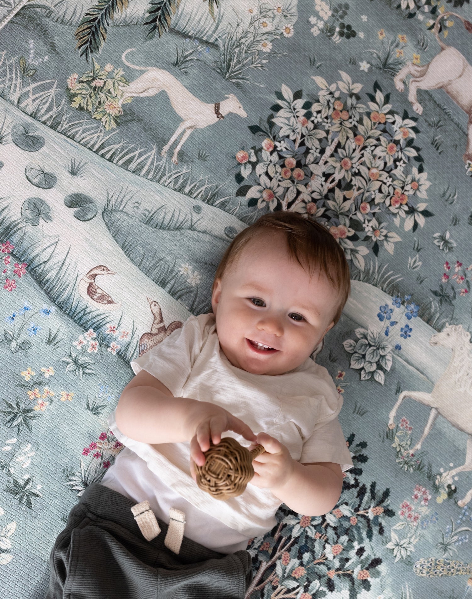 Smiling baby on a Totter + Tumble non-toxic play mat with woodland animal prints - the ultimate in luxury baby products and soft tummy time mats.