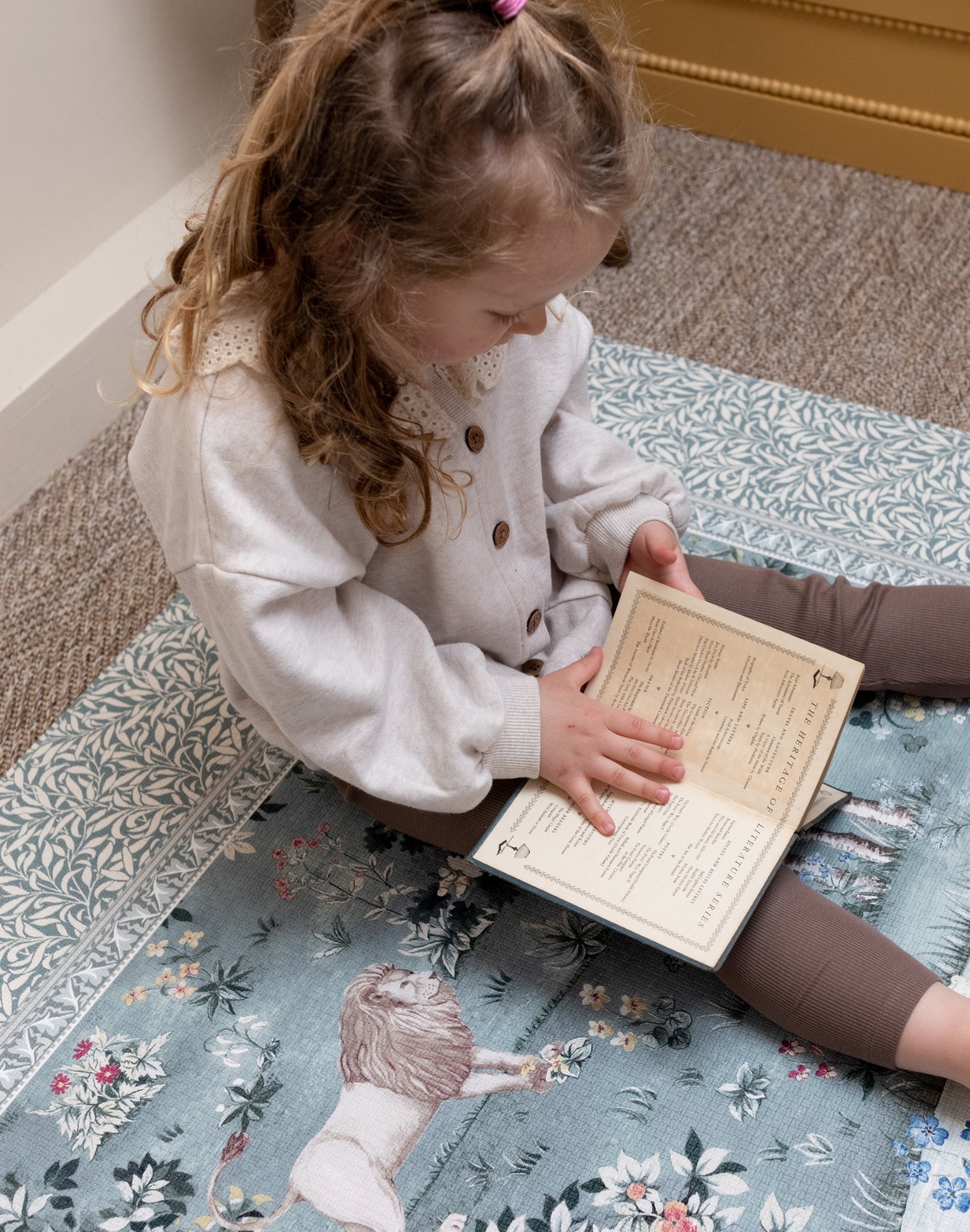 Little girl reads on a William Morris print nursery play mat - practical yet stylish baby product designed for elegant family home aesthetics.