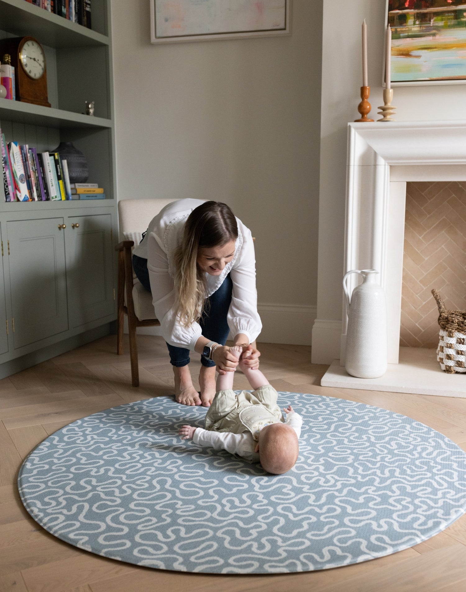 Mum playing with her baby on a patterned blue rug and round playmat in a home setting