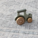 A wooden child's toy tractor lays on a big playmat for children. They playmat has an intricate Persian rug design
