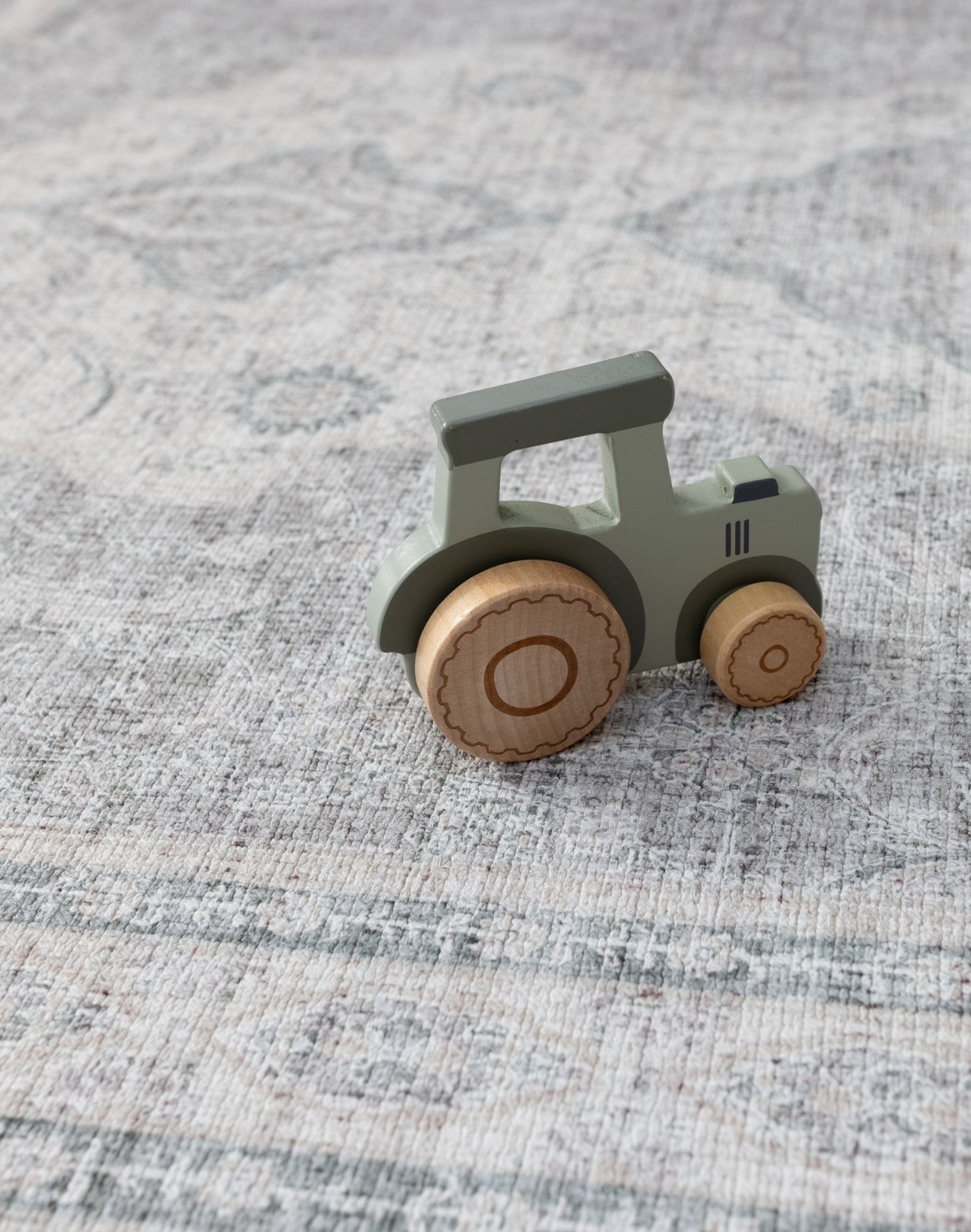 A wooden child's toy tractor lays on a big playmat for children. They playmat has an intricate Persian rug design