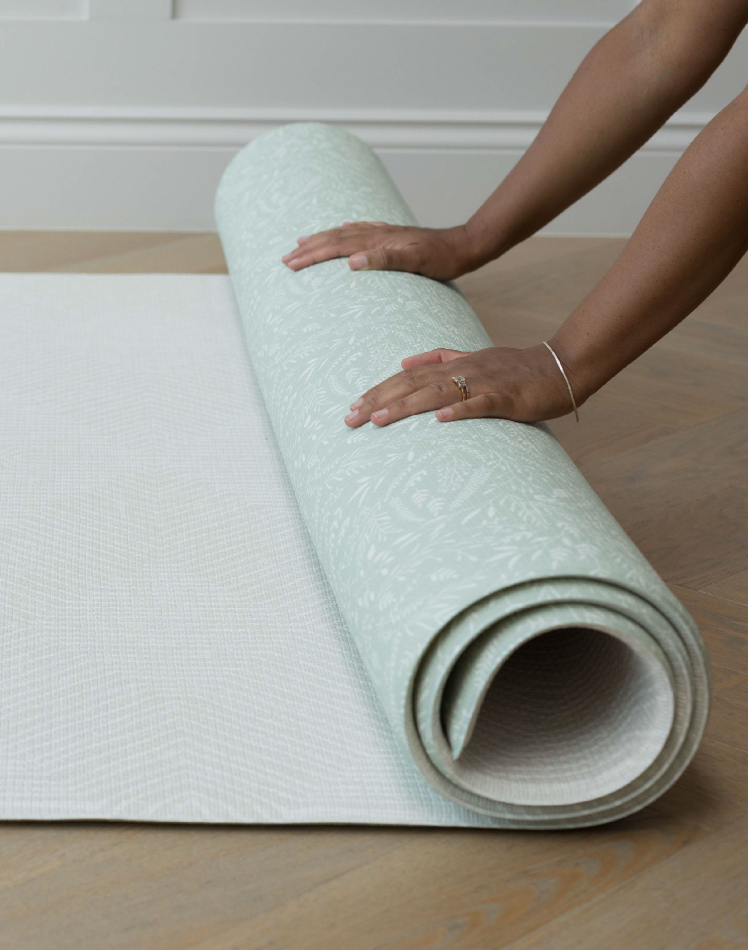 Hands unroll the thick one piece play mat with two complementary designs for modern family hands
