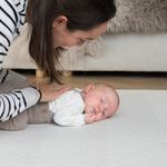 Mum rests gentle hand on the back of a baby laying on a supportive playmat with a gentle design ideal for modern spaces