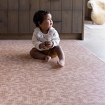 Baby sitting unaided and in comfort on the warm sand orange play mat the Rusa with a textural animal print design
