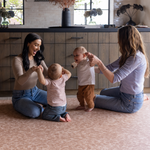 Babies play with their mothers on the stylish orange play mat The Rusa with a gentle animal print motif that looks beautiful in modern homes while providing thick memory foam protection on hard flooring