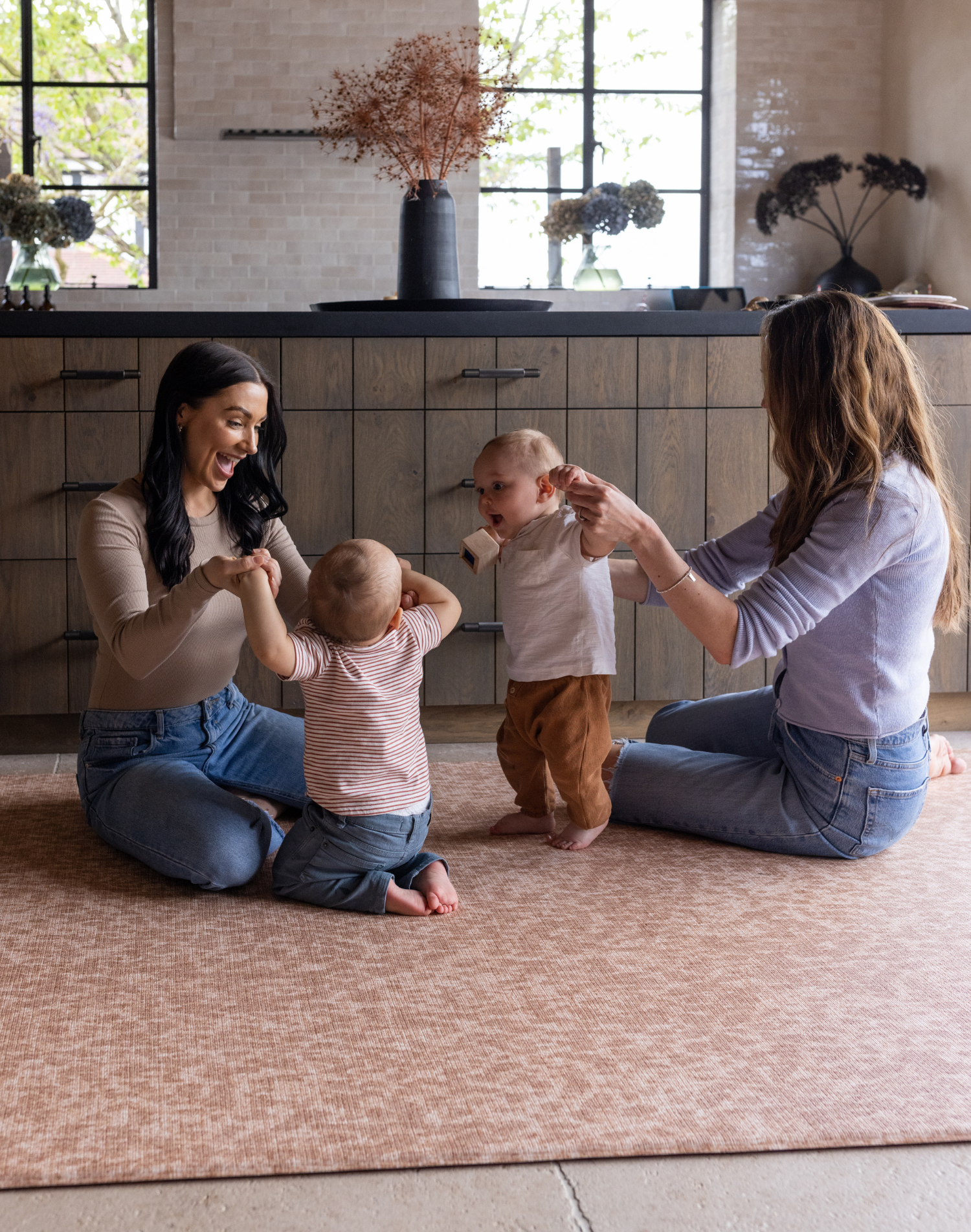 Babies play with their mothers on the stylish orange play mat The Rusa with a gentle animal print motif that looks beautiful in modern homes while providing thick memory foam protection on hard flooring