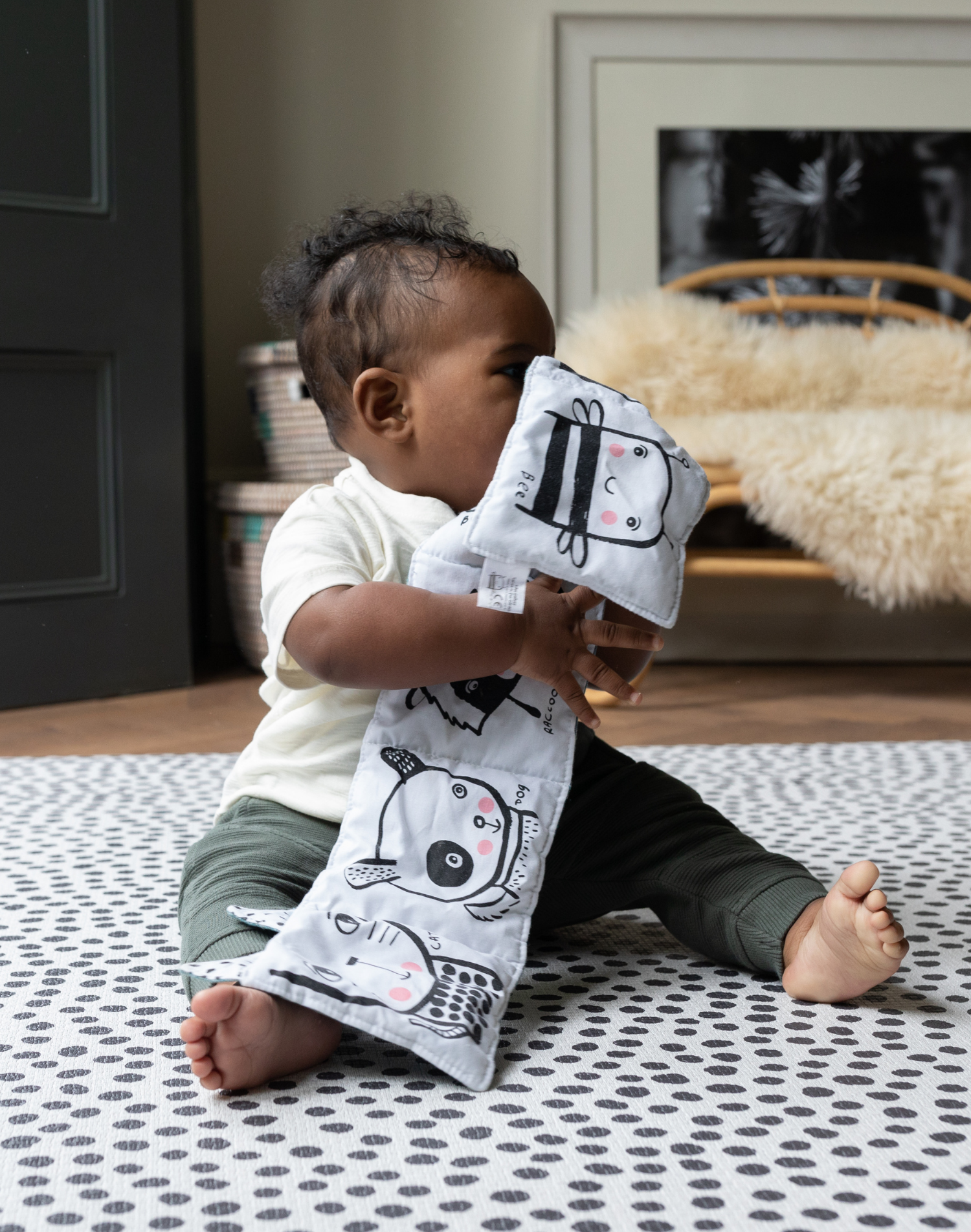 Little boy plays with crinkly book supported on the black and white Scout foam baby mat