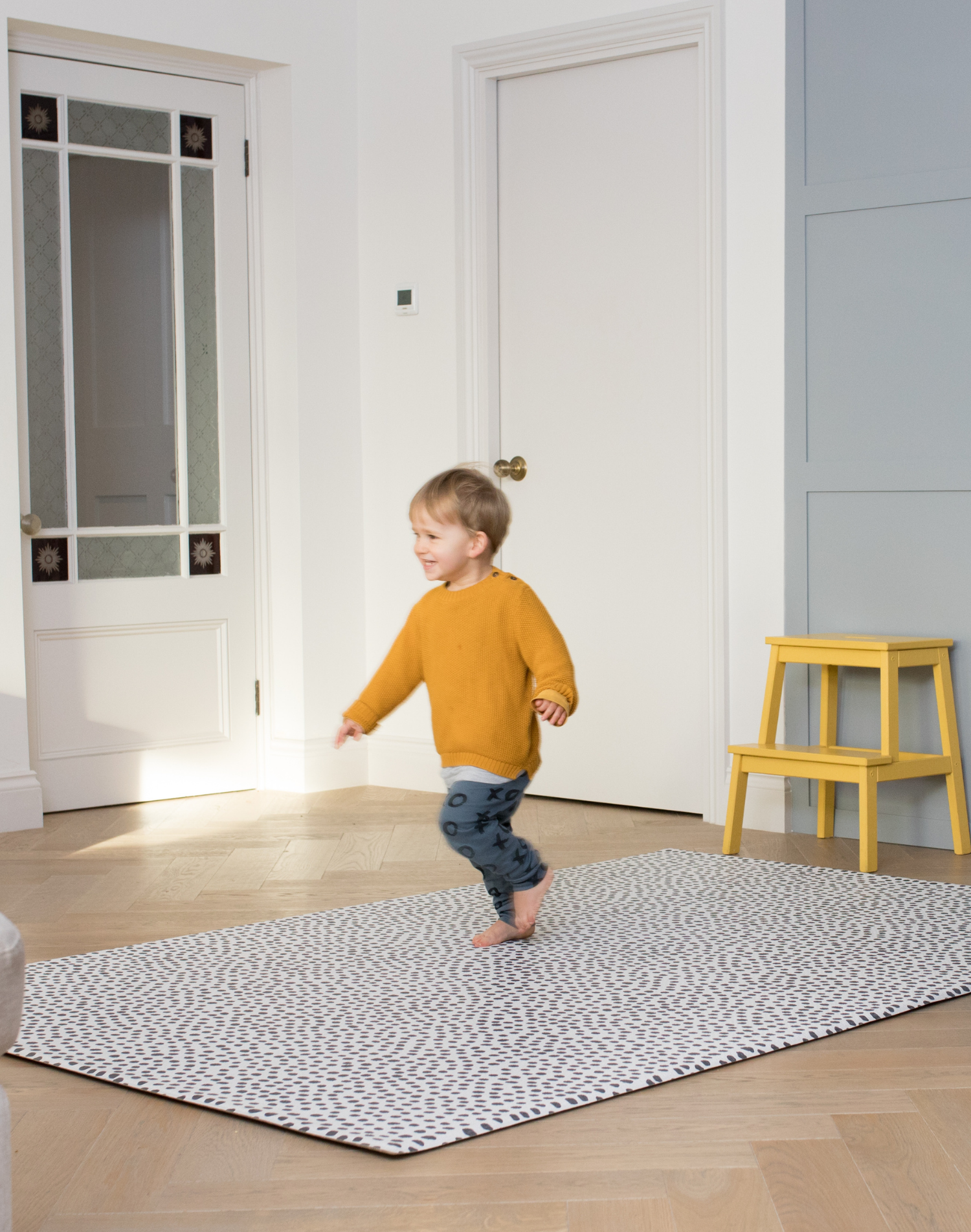 Little boy runs across the extra large playmat by totter and tumble with a polka dot design