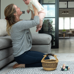 Lady holds up baby during play time on the extra large round play mat by totter and tumble with a polka dot design