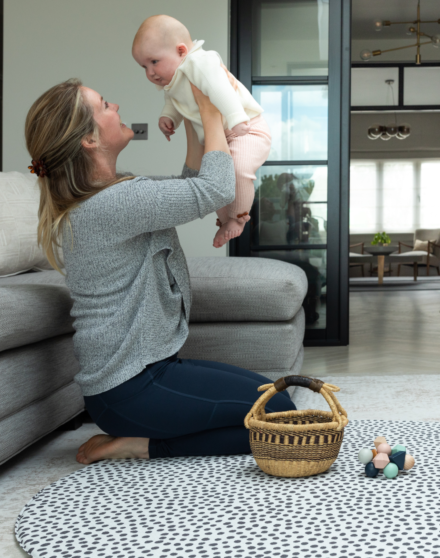 Lady holds up baby during play time on the extra large round play mat by totter and tumble with a polka dot design