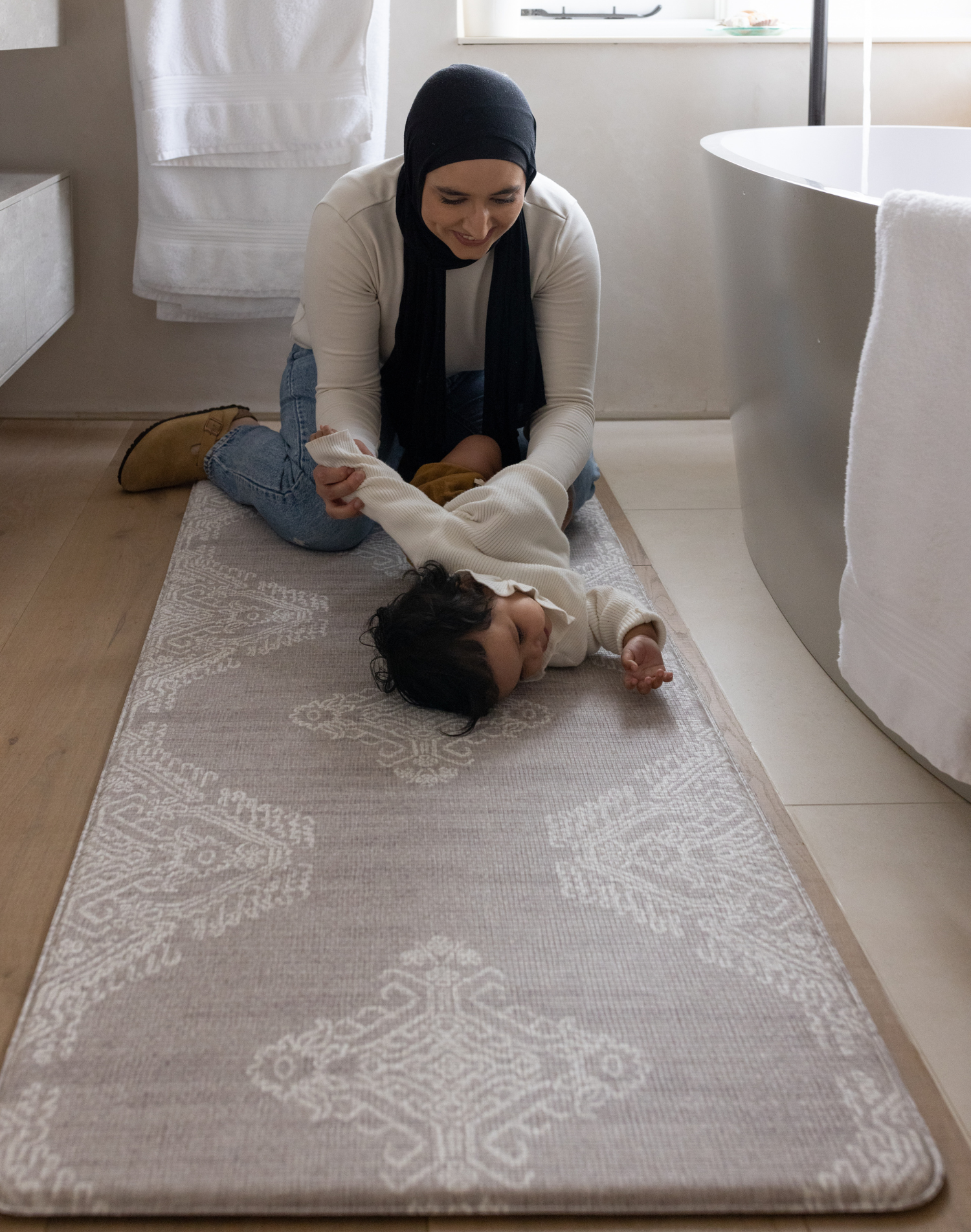 Mother changes baby girl on the large bathroom mat the sepi ideal as a kitchen mat and exercise mat in the home too with a gentle grey design to style seamlessly into modern family interiors