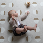 Baby rolls across beige baby playmat with subtle motif reaching for silicone baby toy