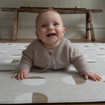 Baby is supported on thick memory foam beige play mat with a subtle motif