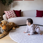 Baby crawls on grey leopard print playmat providing support on the floor during play time with a large soft leopard toy